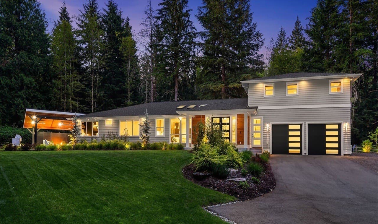Luxury custom home in Snoqualmie, WA built by Hughes Building Co, glowing at dusk against a backdrop of evergreens.